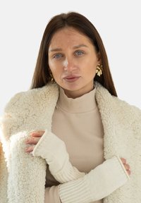 Beżowy prążkowany golf pod puszystym kremowym płaszczem, w połączeniu z kremowymi rękawiczkami bez palców, wykonanymi z tkaniny o teksturowanej powierzchni i miękkim wykończeniu.