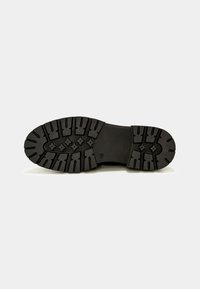 Semelle de chaussure en caoutchouc noir avec des rainures profondes et un motif d'adhérence distinctif. Surface plate avec un centre lisse et des bords surélevés.