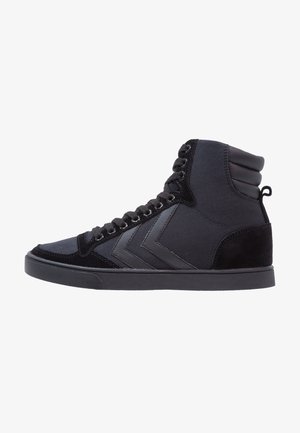Zapatilla negra de caña alta con cordones en la parte delantera, cuello acolchado en el tobillo y diseño en forma de chevrón en el lateral, suela plana.