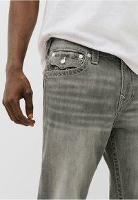 Jeans din denim gri cu decolorare subtilă, design cu cinci buzunare și accesorii din argint. Detalii cusute pe buzunare, croială conică și talie medie.