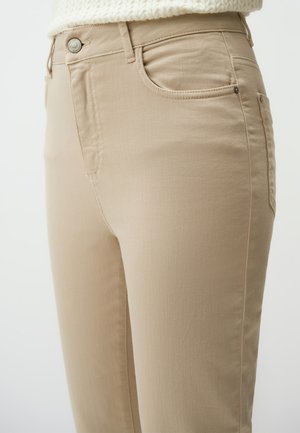 Beżowe dżinsy z dopasowanym krojem, z przednimi kieszeniami, metalowym zapięciem na guzik i minimalnymi detalami ściegów dla gładkiego wykończenia.
