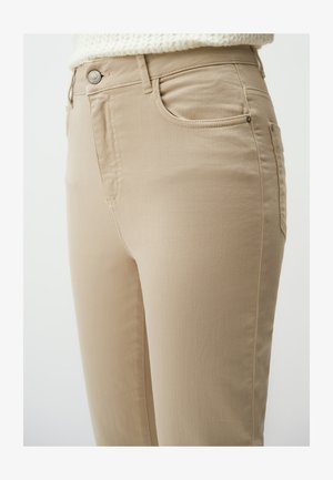 Beżowe dżinsy z dopasowanym krojem, z przednimi kieszeniami, metalowym zapięciem na guzik i minimalnymi detalami ściegów dla gładkiego wykończenia.