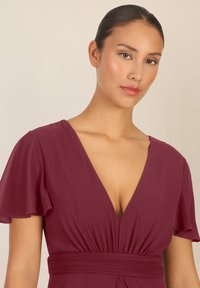 Bordeaux jurk met een diepe V-hals en uitlopende korte mouwen. Elastische taille en zachte, vloeiende stof zorgen voor een soepele silhouet.