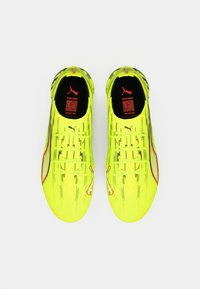 Jaskrawożółte korki piłkarskie z fakturowaną cholewką, podpisami i czerwonymi akcentami. Charakteryzują się smukłym wzorem z wyraźnym logo na języku.