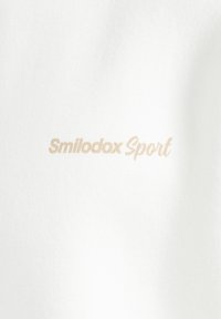 Tessuto bianco con testo beige che recita "Smilodox Sport" stampato sopra.