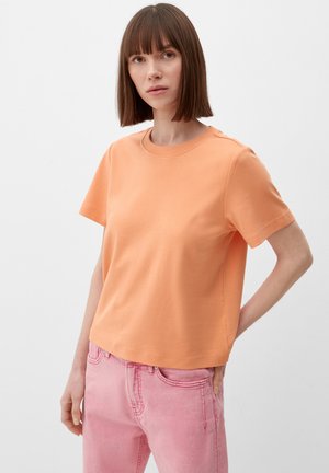 T-shirt à manches courtes, col rond en coton doux couleur pêche. Conçu avec une coupe détendue et une texture lisse ; porté avec un jean en denim rose.