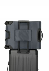 Borsa da viaggio grigia in tessuto con manico retrattile, posizionata sopra una valigia rigida nera con scanalature verticali.