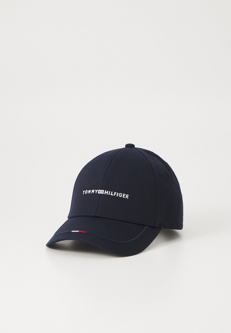 Mørkeblå baseballcap lavet af stof med en buet skygge, prydet med "TOMMY HILFIGER" i hvid broderi og et lille rødt og hvidt accent ved skyggen.