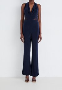 Mörkblå jumpsuit med draperad halsringning, nätutskärningar i midjan och utsvängda ben. Tillverkad av ett mjukt, stretchigt tyg.