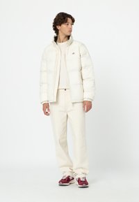 Chaqueta tipo plumón en color crema, con puños y cuello acanalados; combinada con pantalones crema y zapatillas color berenjena; diseño minimalista y ajuste relajado.