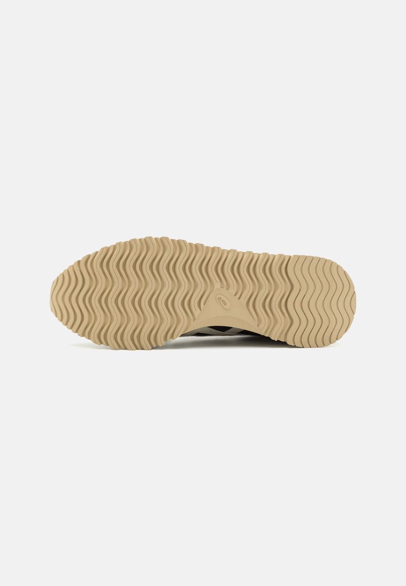 Semelle en caoutchouc avec un motif ondulé, de couleur beige et une surface texturée. Présente un petit logo près de la zone de l'arche.