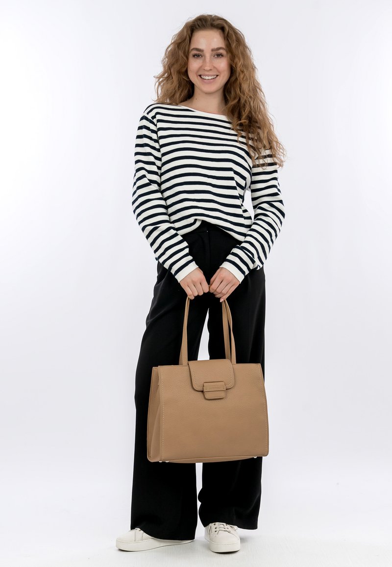 Sac à main en cuir beige avec une forme structurée, une poignée supérieure et une fermeture à rabat à l'avant, associé à une chemise à manches longues rayée et un pantalon noir.