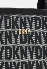 Gros plan sur un tissu texturé noir et gris avec un motif répétitif du logo "DKNY" et de petites lettres dorées "DKNY" sur un sac.