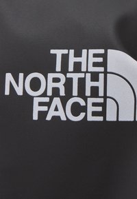 Czarna tkanina z logo "THE NORTH FACE" w dużych białych literach, z charakterystycznym wzorem stylizowanego półkopu, gładka faktura.