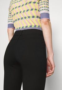 Stickad topp med flerfärgade vågmönster i gult, rosa och blått, i kombination med figurnära svarta byxor med en slät yta och sömdetaljer.
