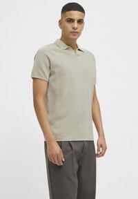 Lys grå polo skjorte med teksturert design, kort ermer og V-hals, kombinert med løstsittende mørk grå bukser.