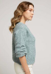 Pull en maille texturée bleu clair avec un design à côtes, col rond et manches mi-longues, associé à un pantalon blanc ajusté.