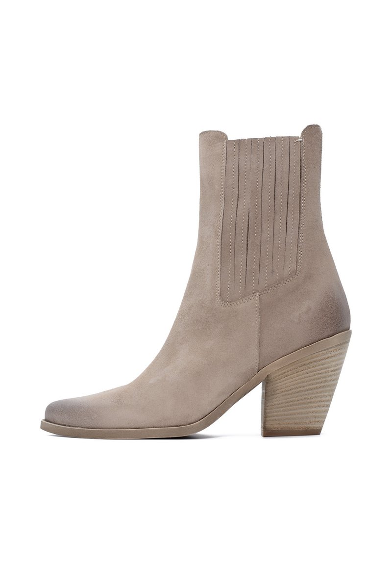 Stivaletto in suede beige chiaro con punta affusolata e dettagli a coste verticali. Presenta un tacco impilato e strutturato per maggiore stabilità.