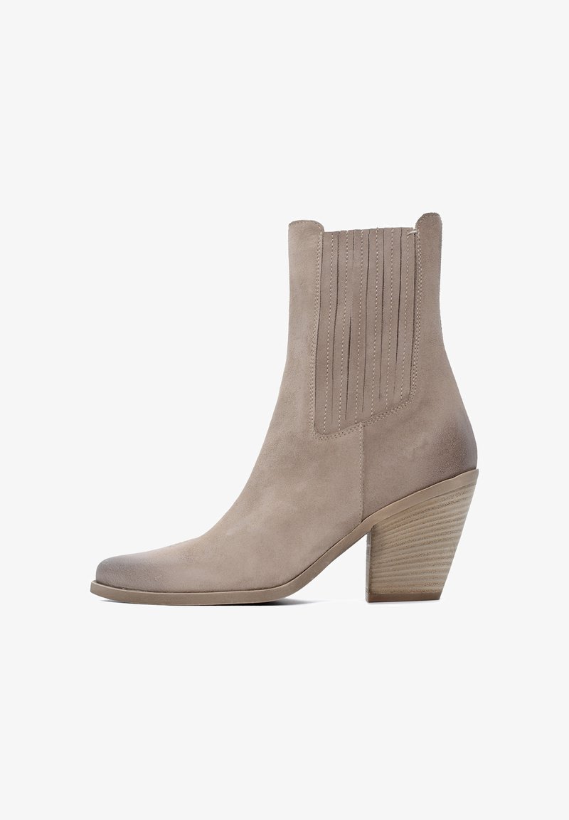 Stivaletto in suede beige chiaro con punta affusolata e dettagli a coste verticali. Presenta un tacco impilato e strutturato per maggiore stabilità.