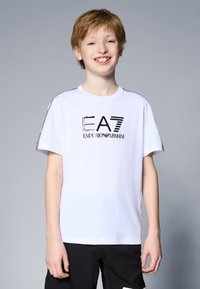Camiseta de algodón blanca con un logo negro de EA7 Emporio Armani en el frente y acentos texturizados en los hombros. Mangas cortas.