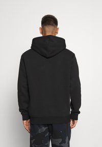 Czarna hoodie z prostym wzorem, z kangurzą kieszenią, ribbed rękawami i teksturowanym materiałem. Widoczne szwy na dolnej krawędzi.
