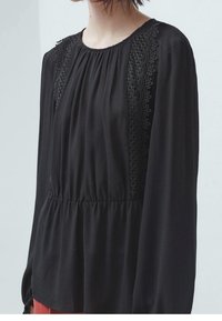 Blusa nera a maniche lunghe con pieghe e dettagli in pizzo sulle spalle, caratterizzata da una vita arricciata e una texture di tessuto liscia.
