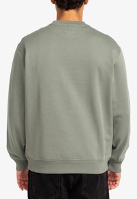 Groene sweatshirt met een ronde hals, geribbelde manchetten en zoom. De stof lijkt zacht en glad, met een eenvoudig ontwerp en minimale details.
