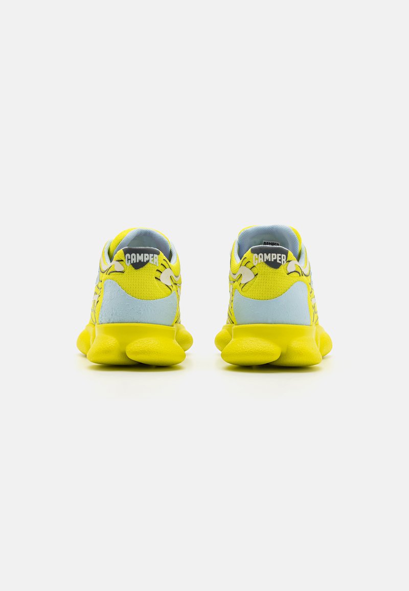 Żółte sneakersy z teksturowanym materiałem, niebieskimi akcentami, grubą podeszwą oraz brandingiem "Camper" na pięcie i języku.