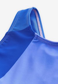 Haut de maillot de bain présentant une combinaison de teintes bleu foncé et clair, texture lisse et couture contrastante rose le long des bords.