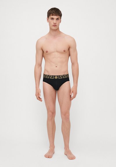 Schwarze Slips mit einem goldenen, gemusterten Bund und einem Medusa-Logo. Der Stoff wirkt glatt und bietet eine enge Passform.