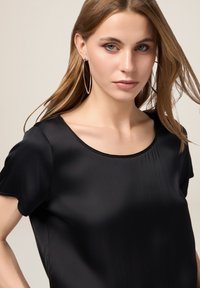 Top in satin nero con maniche corte e scollatura tonda. Texture liscia e design minimalista. Nessun motivo o hardware visibile.