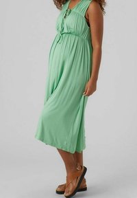 Vestido sin mangas de color verde menta con cintura fruncida y detalle de ojal. Tela suave y ligera con un diseño fluido y un dobladillo hasta la rodilla.