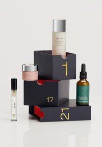Ułożone produkty do pielęgnacji skóry w ciemnych pudełkach z czerwonym wnętrzem; w tym butelka toniku, słoik z kremem oraz serum z pipetą.