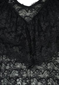 Svart spetstopp med en vågig design och intrikata blommönster. V-ringad hals och textil med struktur skapar ett lager av visuell intress.