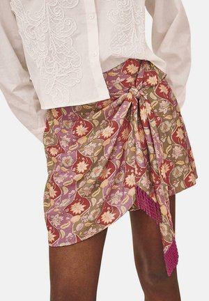 Falda envolvente floral con patrones en burdeos, verde y crema. Se ata en la cintura, con un remate texturizado en el dobladillo. Combinada con una blusa blanca bordada.