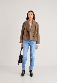 Chaqueta marrón de lana cruzada con grandes solapas, combinada con vaqueros azul claro y botines negros, sujetando un bolso negro.