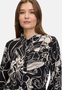 Svart och crème-färgad blommig skjorta med krage. Har en avslappnad passform och intrikata blommönster på ett lätt tyg.