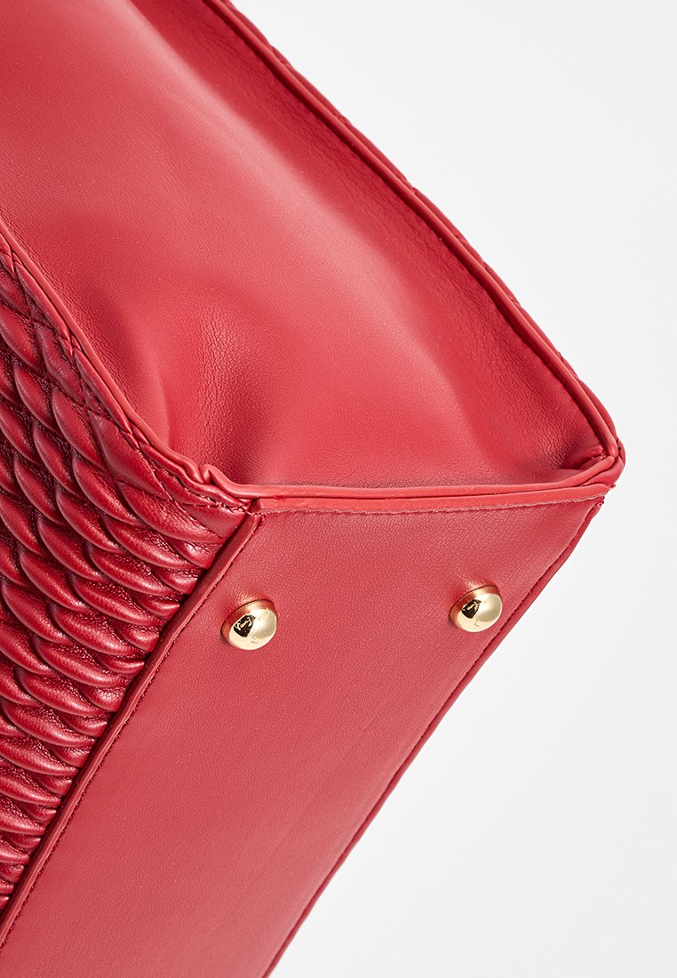 Sac en cuir rouge avec un motif tissé texturé d'un côté, une surface lisse de l'autre, et des accents en métal doré.