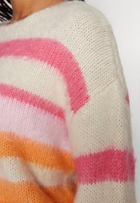 Sweter w paski z poziomymi pasami w kolorze różowym, pomarańczowym i kremowym. Wykonany z miękkiej, fakturowanej przędzy o luźnym kroju i dzianinowym wzorze.