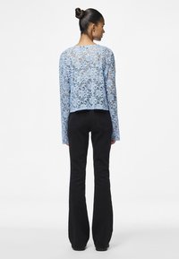 Light blue lace long-sleeve top with floral pattern, cropped design, paired with black flared jeans and black footwear.