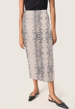 Femme portant une jupe taille haute longueur cheville avec un motif serpent gris et noir et des ballerines à bout pointu avec bride noire arrière.