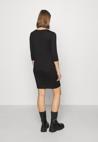 Abito nero attillato con maniche a tre quarti, realizzato in tessuto liscio. Presenta un scollo rotondo e lunghezza a metà coscia. Indossato con stivaletti neri alla caviglia.