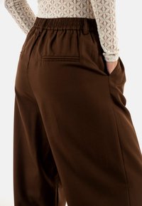 Bruine broek met een elastische tailleband, voorzien van zijzakken en een gladde textuur. De stof heeft een gestructureerde, op maat gemaakte uitstraling.