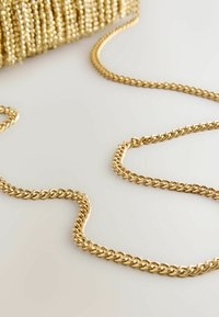 Goldene Kettenriemen mit geflochtenem Design, ruhend auf einer hellen Oberfläche und verbunden mit einer strukturierten goldenen Tasche. Glatte, metallische Oberfläche.