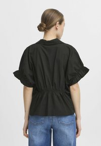 Black cotton blouse with a cinched waist, short puff sleeves, and a straight collar, worn with light blue denim jeans.
