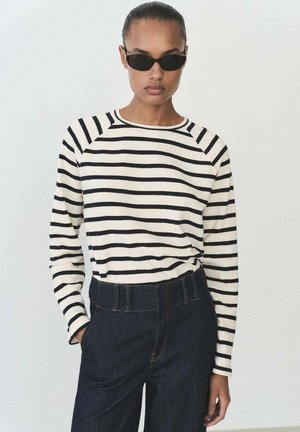 Randig långärmad topp i kräm och svart, i bomullstyg, med rund halsringning och raglanärmar, kombinerad med mörka högmidjade jeans.