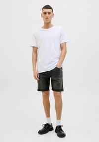 Tricou alb cu mânecă scurtă, pantaloni scurți din denim închis cu margini răsucite, pantofi negri cu șiret, și șosete albe, stând pe un fundal simplu.