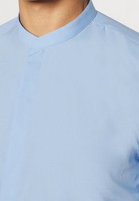 Lichtblauw shirt met korte mouwen, met een bandkraag, een soepele textuur en een strak ontwerp met minimale stiksels, ideaal voor casual draag.