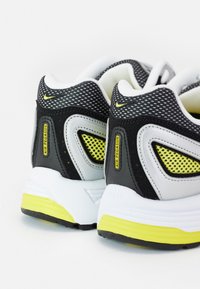 Sorte, grå og gule Nike Air Pegasus-sneakers, der viser bag- og sidedetaljer med mesh og mærkede accenter på hvide såler.