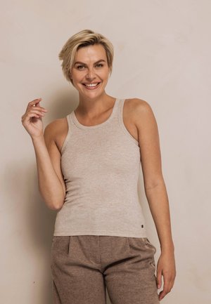 Beige ribbed tank top with a round neckline and wide straps, paired with brown trousers featuring a subtle textured pattern.